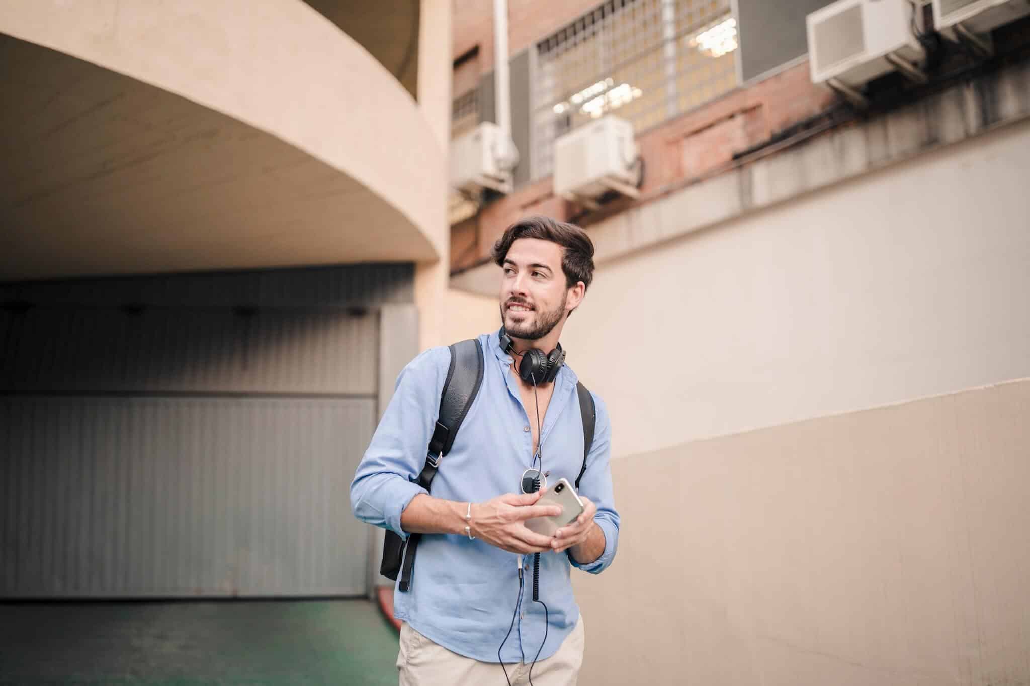 Man wearing headphones and carrying smartphone outdoors.